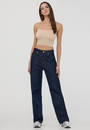 Jeans in denim blu scuro, a vestibilità ampia, con cinque tasche, dettagli cuciti e una chiusura con un singolo bottone frontale. Abbinati a un top corto beige.