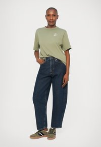 Camiseta de algodón verde oliva de manga corta y cuello redondo, combinada con jeans de mezclilla azul de tiro alto y zapatillas olivas con rayas negras.