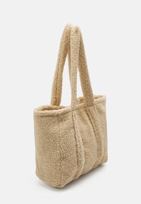 Beige nepbont tote bag met twee lange banden, rechthoekige vorm en gestikte details langs de randen. Zachte textuur.