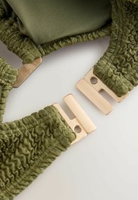 Olivgrüner elastischer Stoff mit strukturiertem, gerafftem Design und goldfarbenen Metallverschlüssen zum Schließen. Glatte Oberfläche.