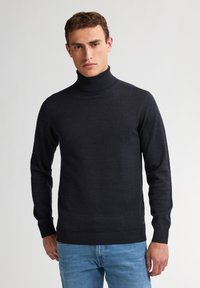 Ciemnoszary sweter z golfem, wykonany z gładkiej dzianiny, z długimi rękawami oraz ściągaczami przy mankietach i u dołu. Noszony z jasnoniebieskimi dżinsami.