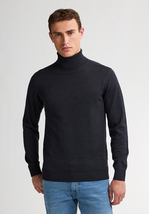 Jersey de cuello alto de color gris oscuro, hecho de un tejido de punto suave, con mangas largas y puños y dobladillo de canalé. Llevado con jeans de color azul claro.