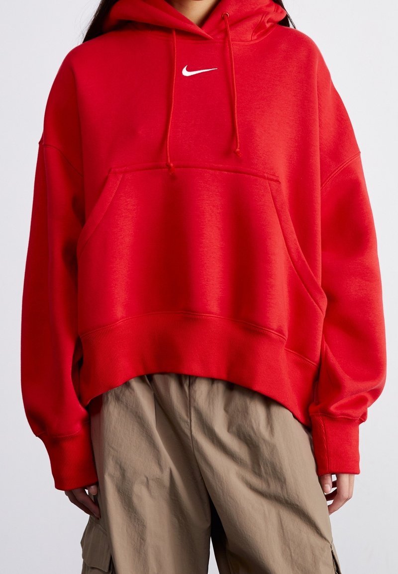 Röd oversized hoodie gjord av bomullsmaterial. Har en framficka av kangurustil och en vit logotyp på bröstet. Texturerade ribbade muddar.