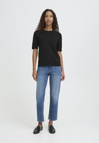 Haut noir à manches courtes assorti à un jean en denim bleu clair à jambes droites et des mocassins noirs, présenté sur un fond blanc uni.