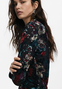 Mustakirjuline pluus, mis sisaldab mitmevärvilisi lilli punases, sinises ja kreemis. Pikkade varrukatega, tekstuurse mustriga ja ülikitsas disain.