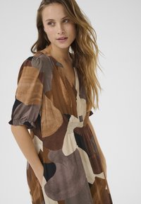 Brown abstract patterned dress with short puff sleeves, V-neck, gathered waist, and side pockets; made from lightweight fabric.