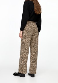 Byxor med leopardtryck i beige och svart, med hög midja och rullad kant, tillsammans med svarta ankelskor.