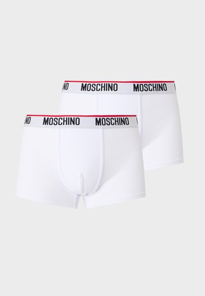 Dwie białe bokserki Moschino z czarnym logo na elastycznych pasach w talii z czerwonym obszyciem, prezentowane na jasnym tle.