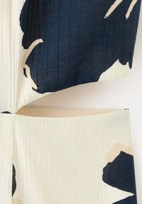 Gros plan sur un tissu beige et marine avec de grands motifs floraux abstraits et un détail découpé entre deux sections de tissu.