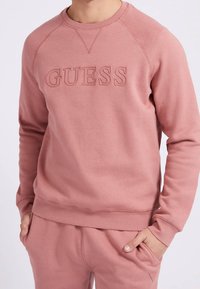 Lyserød pullover sweatshirt med præget "GUESS"-logo, lavet af en blød bomuldsblanding, med rund hals og ribstrikkede ærmegab.