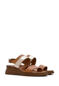Sandalias de cuña marrones con una correa de acento dorado metálico, diseño de punta abierta y hebilla ajustable en el tobillo, con un material superior texturizado.