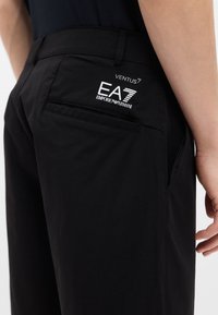 Μαύρο ελαφρύ παντελόνι από λείο υλικό, με πίσω τσέπη που φέρει λευκό λογότυπο με την επιγραφή "EA7 EMPORIO ARMANI" και κομψό σχέδιο.