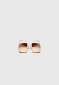 Beige sandal skor med klack, med ett brett rem och en dekorativ spänne. Slät material med en enkel, minimalistisk design.