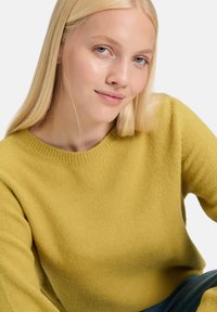 Senfgelbes Strickpullover mit einem gerippten Rundhalsausschnitt und langen Ärmeln, der eine weiche Textur und eine lockere Passform aufweist.