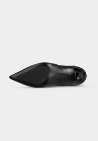 Chaussure en cuir noire à bout pointu vue de la semelle, montrant une semelle lisse avec une petite zone texturée près du talon.