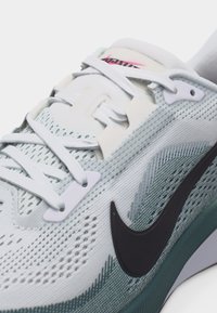 Κοντινό πλάνο άσπρου και ανοιχτού γαλάζιου αθλητικού παπουτσιού με μαύρο λογότυπο Nike και άσπρα κορδόνια, που δείχνει λεπτομερές πλεκτό υλικό και ετικέτα στη γλώσσα.