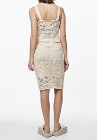 Vestido de punto con silueta ajustada, que presenta detalles de ganchillo en un color beige claro. Tirantes gruesos y diseño hasta la rodilla.