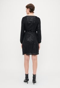 Vestido negro con lentejuelas y mangas largas, cintura ajustada, y un dobladillo que cae a mitad del muslo. Usado con botas de tobillo. Superficie texturizada y brillante.