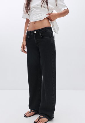 Jean noir à jambes larges en denim, avec taille haute, poches avant et fermeture à boutons. Associé à un haut blanc court.