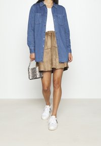 Jeansskjorta, brun mockaskjorta, silverväska med ormskinnsmönster och vita sneakers. Har knäppning och fickor på skjortan.