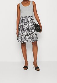 Grå linne, svart blommig kjol med vita rosor, knälång, något utsvängd, ihop med en svart kuvertväska och svarta klacksandaler.