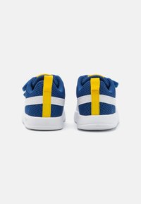 Zapatillas de malla azules con acentos blancos, bucles amarillos en el talón y un diseño de perfil bajo. Cuenta con un cuello acolchado y una suela texturizada y ligera.