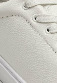 Sneaker bianca in pelle con finitura testurizzata, dotata di lacci in tessuto, occhielli rotondi e una suola in gomma bianca liscia.