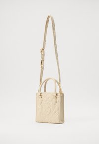 Beżowa pikowana torebka o sztywnej formie, z podwójnymi uchwytami u góry oraz długim, regulowanym paskiem. Złote akcenty metalowe podkreślają design.