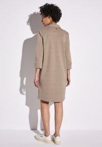 Beige, gemêleerde shirtjurk met een kraag, driekwartmouwen en knoopdetails, gecombineerd met witte sneakers voor een casual look.