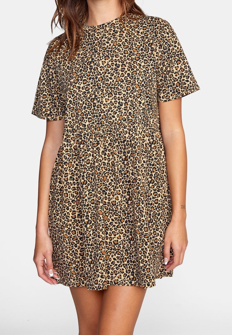 Femme portant une mini-robe à manches courtes à imprimé léopard avec une taille froncée, debout devant un fond blanc uni.