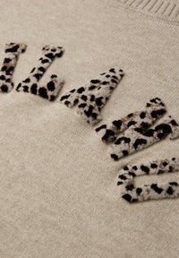 Beżowy sweter z teksturowanymi literami w panterkę, ozdobnie naszywanymi, wykonany z miękkiego materiału, z prążkowanym dekoltem.
