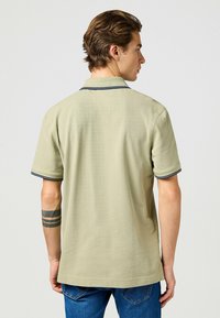 Olivgrön polo med krage, med marinblå detaljer på kragen och ärmarna. Korta ärmar, slät textur och avslappnad passform.