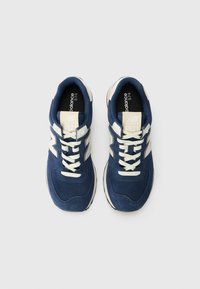 Mörkblå mocka och mesh sneakers med vita accenter och snören. Har en rundad tå och vadderade sulor. Modellnummer 574 synligt.