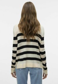 Maglione a righe beige e nero con maniche lunghe, vestibilità morbida, polsini a costine e spacco laterale, abbinato a jeans in denim azzurro chiaro.