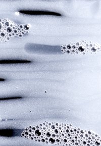 Sitrende overflate med varierende størrelser av bobler; overveiende hvit og transparent med en glatt tekstur, akkompagnert av spredte svarte flekker.