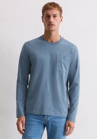 Koszula z długim rękawem, w jasnym niebieskim kolorze, wykonana z bawełny, z okrągłym dekoltem i kieszenią na piersi. Charakteryzuje się luźnym krojem oraz miękką, gładką fakturą.