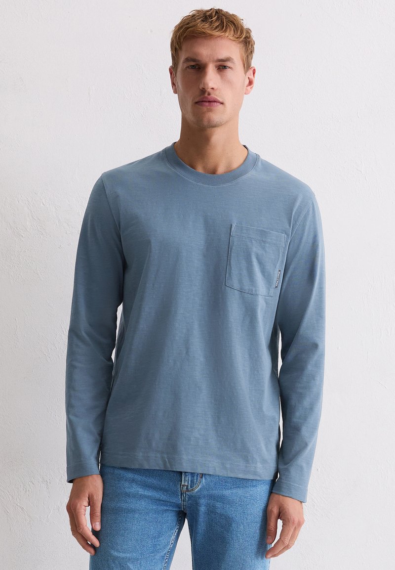 Koszula z długim rękawem, w jasnym niebieskim kolorze, wykonana z bawełny, z okrągłym dekoltem i kieszenią na piersi. Charakteryzuje się luźnym krojem oraz miękką, gładką fakturą.