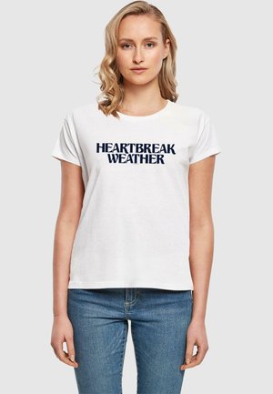 White cotton t-shirt featuring the text "HEARTBREAK WEATHER" in navy blue, short sleeves, rounded neckline, relaxed fit.