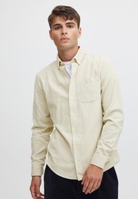 Light yellow button-down shirt made of soft fabric, featuring a chest pocket and a slightly curved hem. Long sleeves with buttoned cuffs.