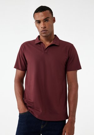 Bordeaux polo-shirt med krave og korte ærmer, der har en glat tekstur og en afslappet pasform, parret med mørke denim jeans.