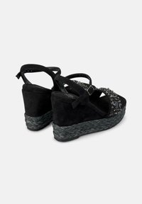 Sandalias de cuña de ante negro con detalles de cuentas y suela de yute trenzado. Cuenta con una correa ajustable en el tobillo y plantilla acolchada.