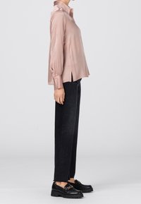 Rosenfärgad satin skjorta med lång ärm, krage och sidofickor, parat med avsmalnande svarta byxor och kraftiga svarta loafers med guld detaljer.