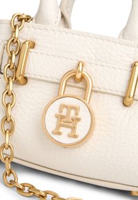 Λευκή δερμάτινη τσάντα με χρυσά μεταλλικά στοιχεία, διαθέτοντας λουρί αλυσίδα και κλειδαριά σχήματος δίσκου με ανάγλυφα λογότυπα.