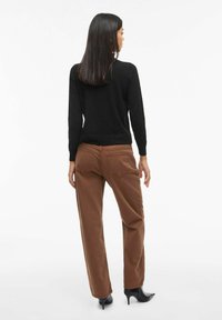 Zwarte trui, bruine brede broek en puntige zwarte hakken. De trui heeft een ronde hals en de broek heeft achterzakken en een zachte textuur.