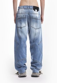 Svijetloplave široke traperice s izbleđenim finišem, koje imaju velike stražnje džepove i crnu oznaku na pojasu.