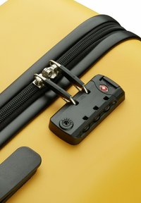 Valigia rigida gialla con superficie testurizzata, zip nera e lucchetto a combinazione approvato dalla TSA con accenti colorati.