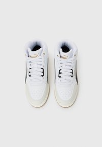 Et par hvite høyhælte Puma-sneakers med svarte side-striper og gull-logo detaljer, sett ovenfra på hvit bakgrunn.