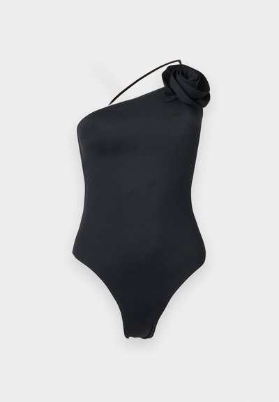 Μαύρο ολόσωμο μαγιό με έναν ώμο, λεπτό ιμάντα και υφασμάτινη λεπτομέρεια τριαντάφυλλου στον ώμο, εμφανίζεται σε απλό ανοιχτό υπόβαθρο.