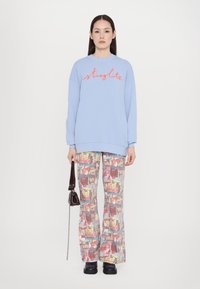 Light blue oversized sweatshirt with red "stiglit" text, paired with flared, patterned pants featuring colorful magazine prints and black platform shoes.