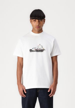 T-shirt de algodão branco com gola redonda, apresentando uma gráfica de uma caminhonete e formas geométricas em cores suaves na parte da frente.